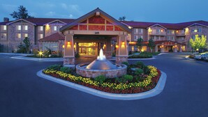 Um hotel com fachada de pedra, uma fonte central e um jardim bem cuidado.