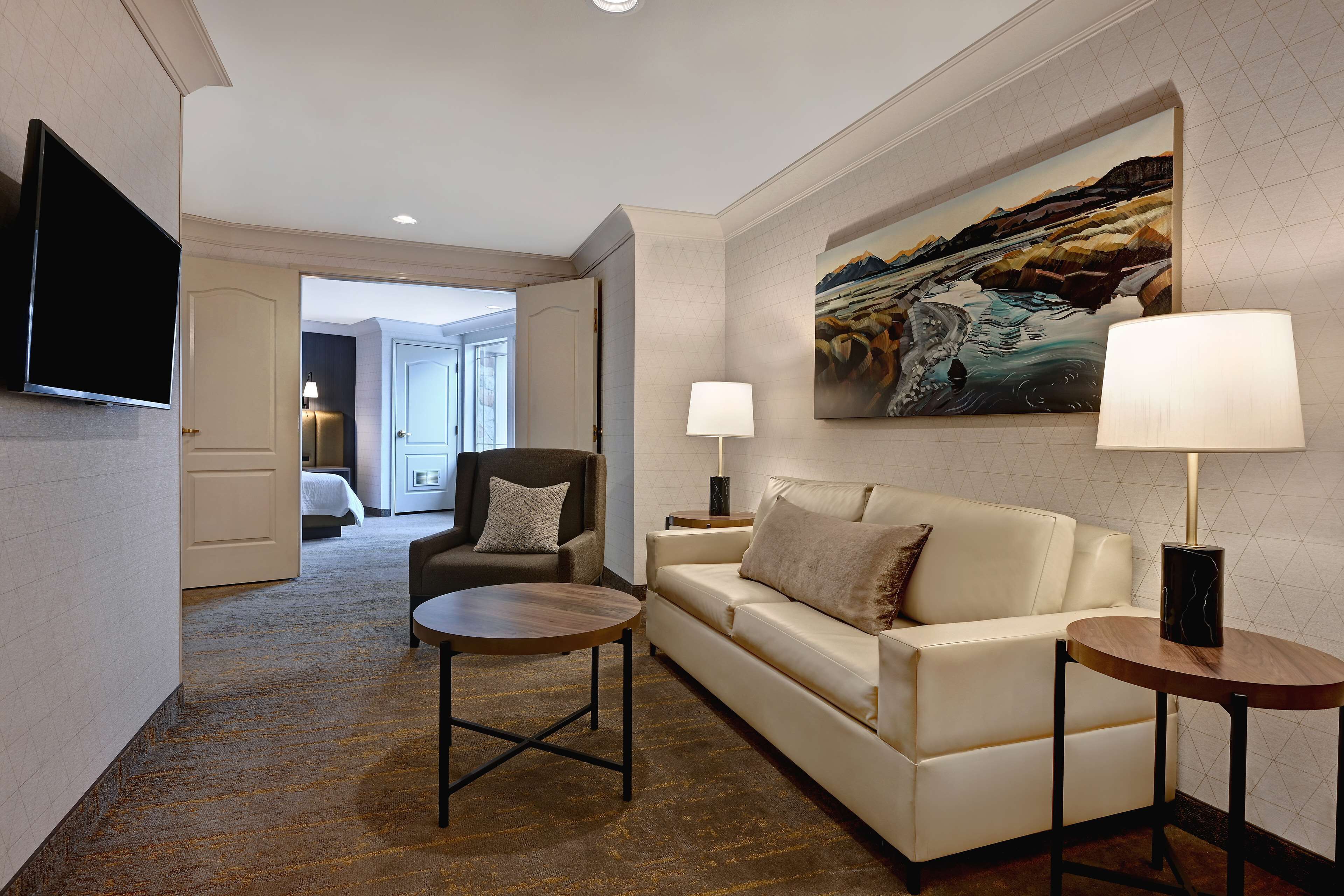 A hotel room with a large bed, a sofa, a coffee table, a TV, and a painting on the wall.
