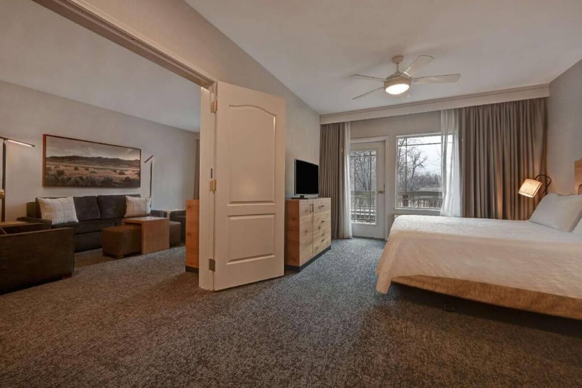 A hotel room with a bed, a TV, a desk, a chair, a sofa, a wardrobe, and a door leading to a balcony.