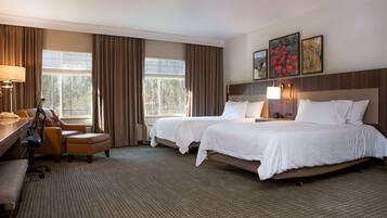 Een hotelkamer met twee bedden, een bureau, een stoel en een raam met gordijnen.