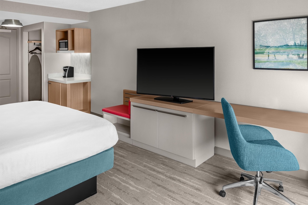 A hotel room with a bed, a desk with a TV, a chair, a microwave, and a wardrobe.