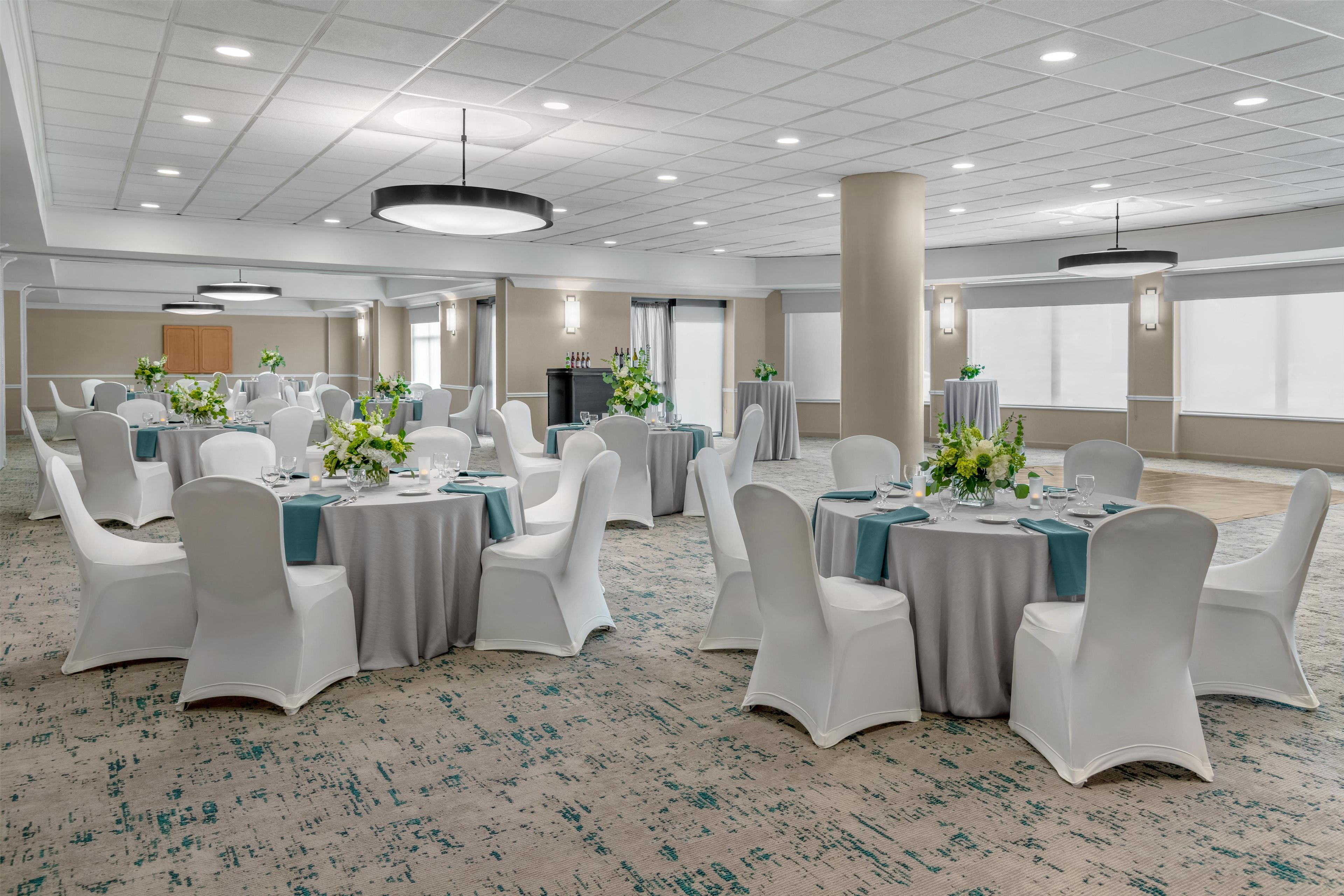 A spacious banquet hall with round tables, white chairs, and floral centerpieces.
