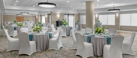 A spacious banquet hall with round tables, white chairs, and floral centerpieces.
