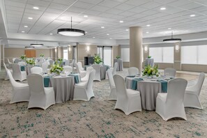 Un amplio salón de banquetes con mesas redondas, sillas blancas y centros de mesa florales.