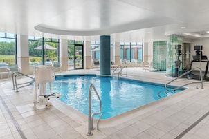 Una piscina interior con agua cristalina, rodeada de sillones de descanso y un muro de vidrio.