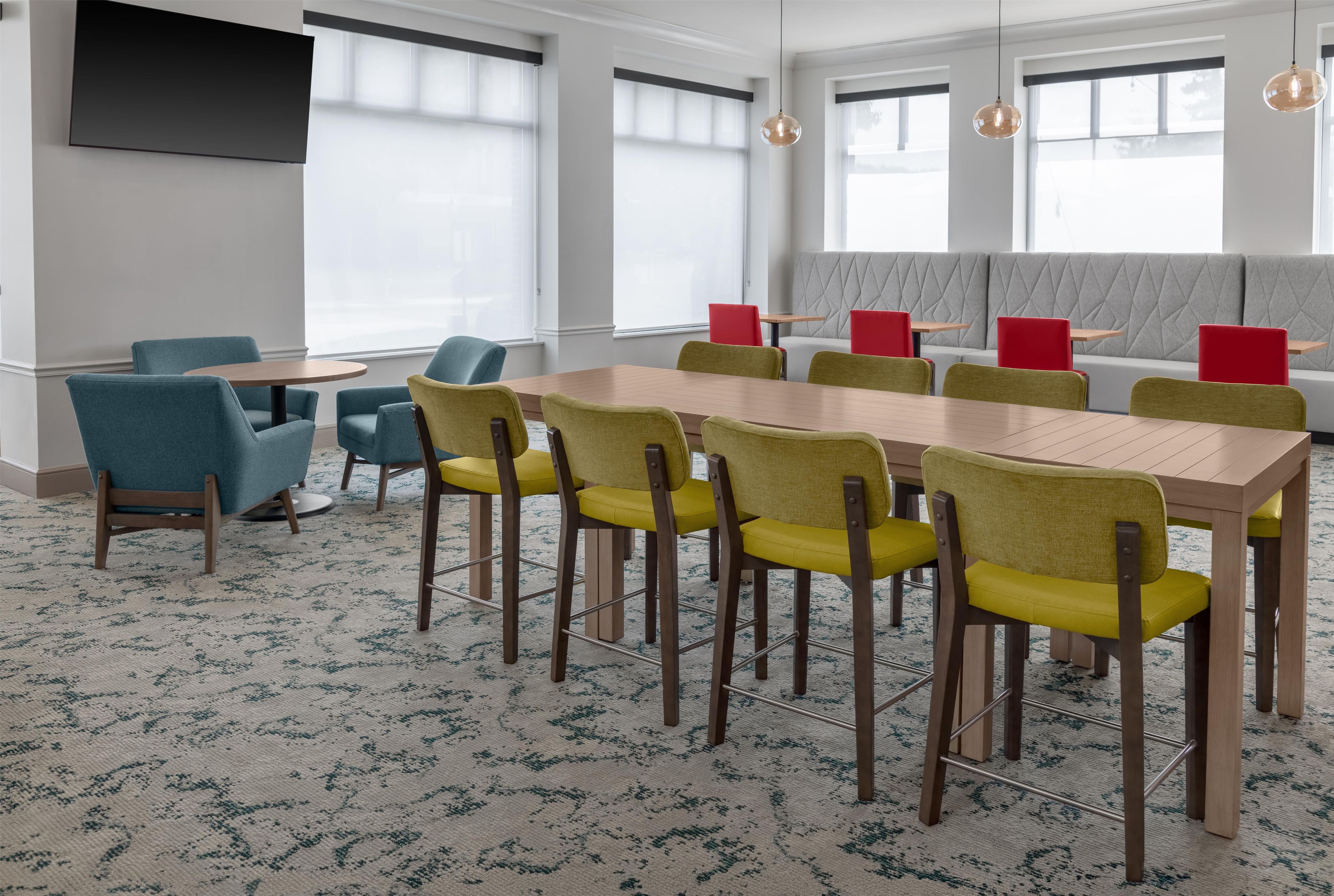 A conference room with a long table, multiple chairs, and a seating area with red chairs.
