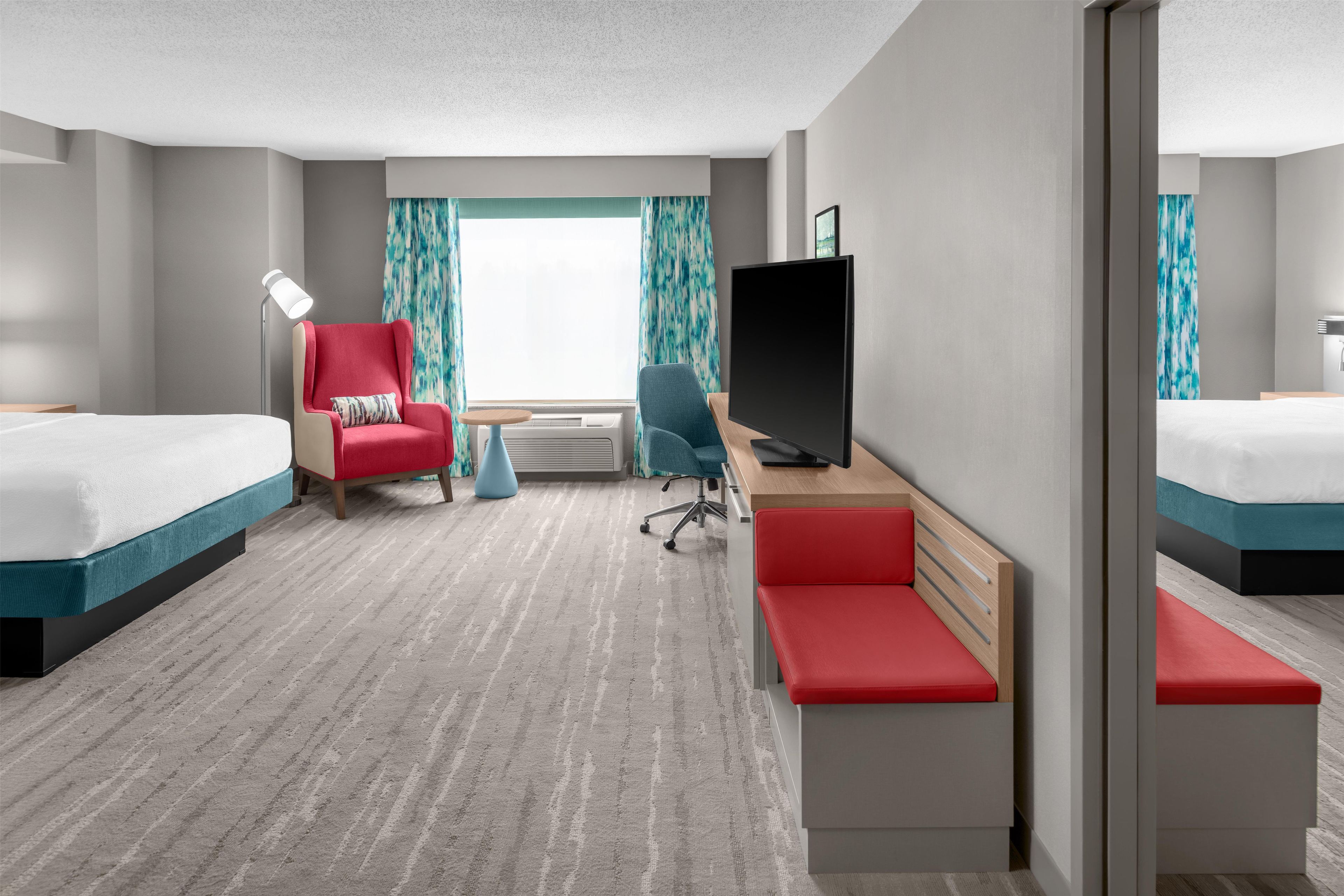 Una habitación de hotel con dos camas, un escritorio con televisor, una silla y una mesita.