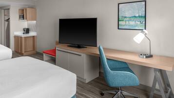 Une chambre d’hôtel avec un lit, un bureau doté d’une télévision, une chaise, une lampe de bureau et un tableau encadré au mur.