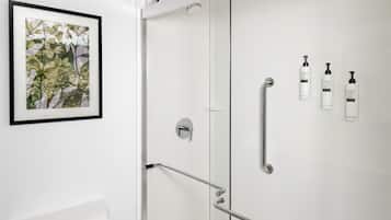 A bathroom with a glass shower door, a framed picture on the wall, and toiletries mounted on the wall.