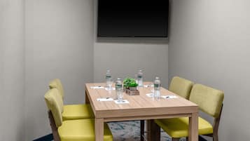 Un salón de conferencias con una mesa de madera, sillas amarillas, un televisor de pantalla plana en la pared y botellas de agua sobre la mesa.