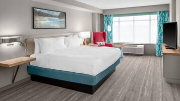 Una habitación de hotel con cama, escritorio, silla, televisor, ventana con cortinas y un cuadro en la pared.