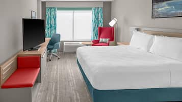 A hotel room with a bed, a desk with a TV, a chair, a desk lamp, and a window with curtains.