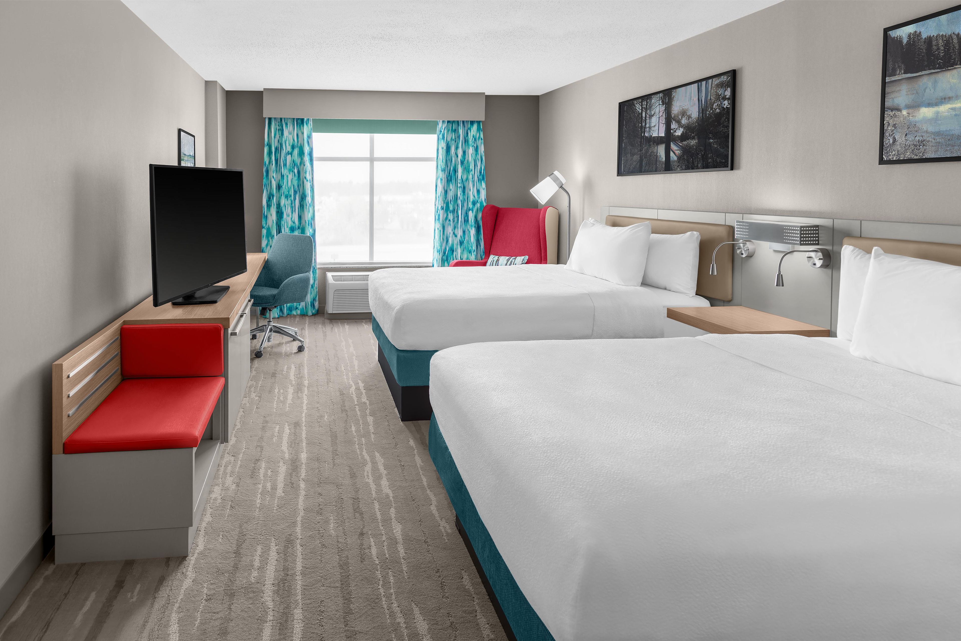 Habitación de hotel con dos camas, televisión, escritorio, silla y ventana con cortinas.