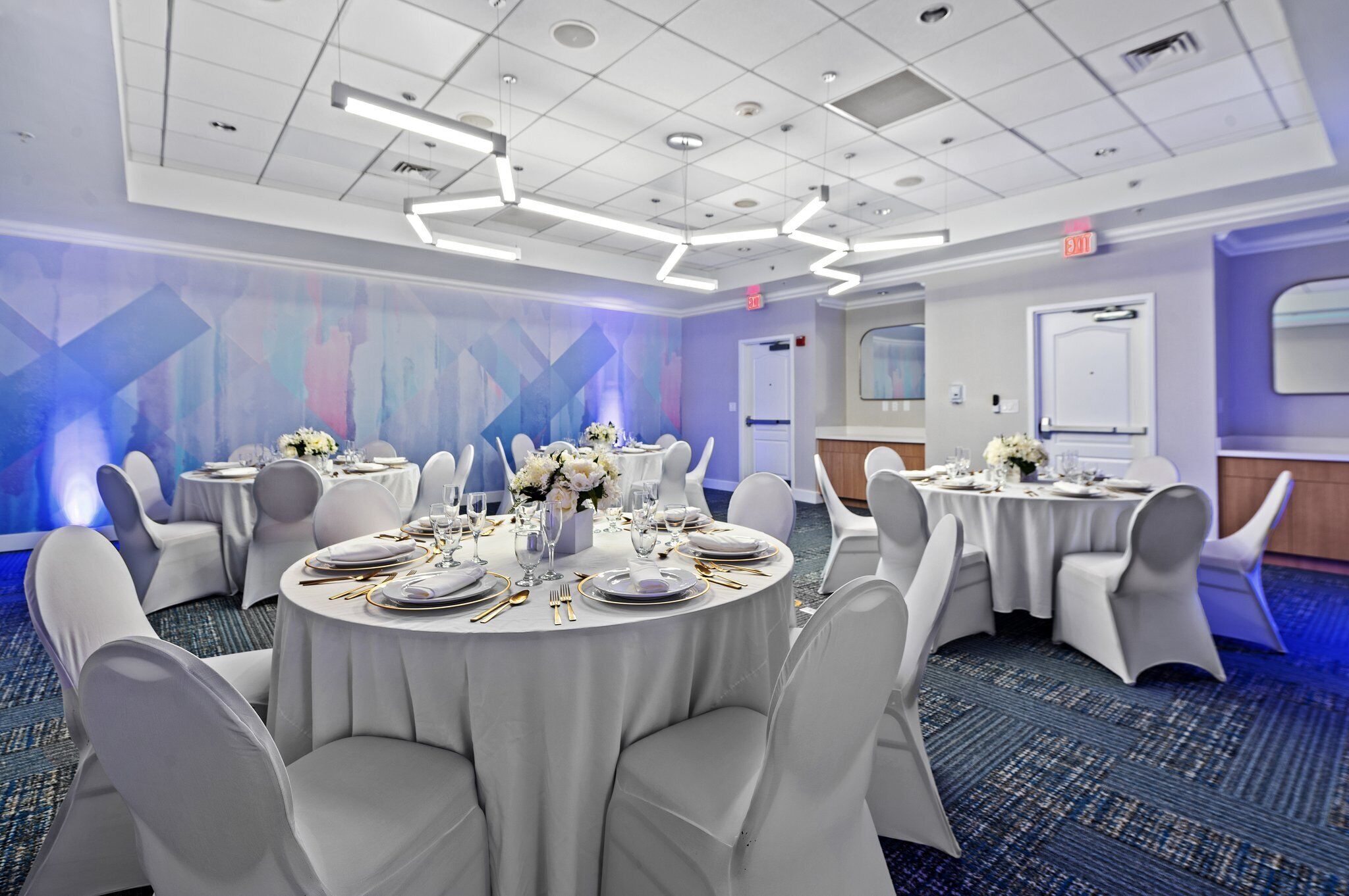 A conference room with round tables, white chairs, and a blue abstract wall design.