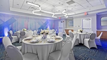 A conference room with round tables, white chairs, and a blue abstract wall design.