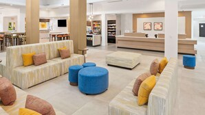 Un hall amplio con techos altos, ventanas grandes y una zona de estar central con sofás y otomanas.