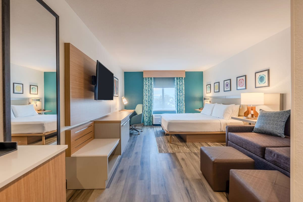A hotel room with two beds, a desk, a sofa, and a large mirror.