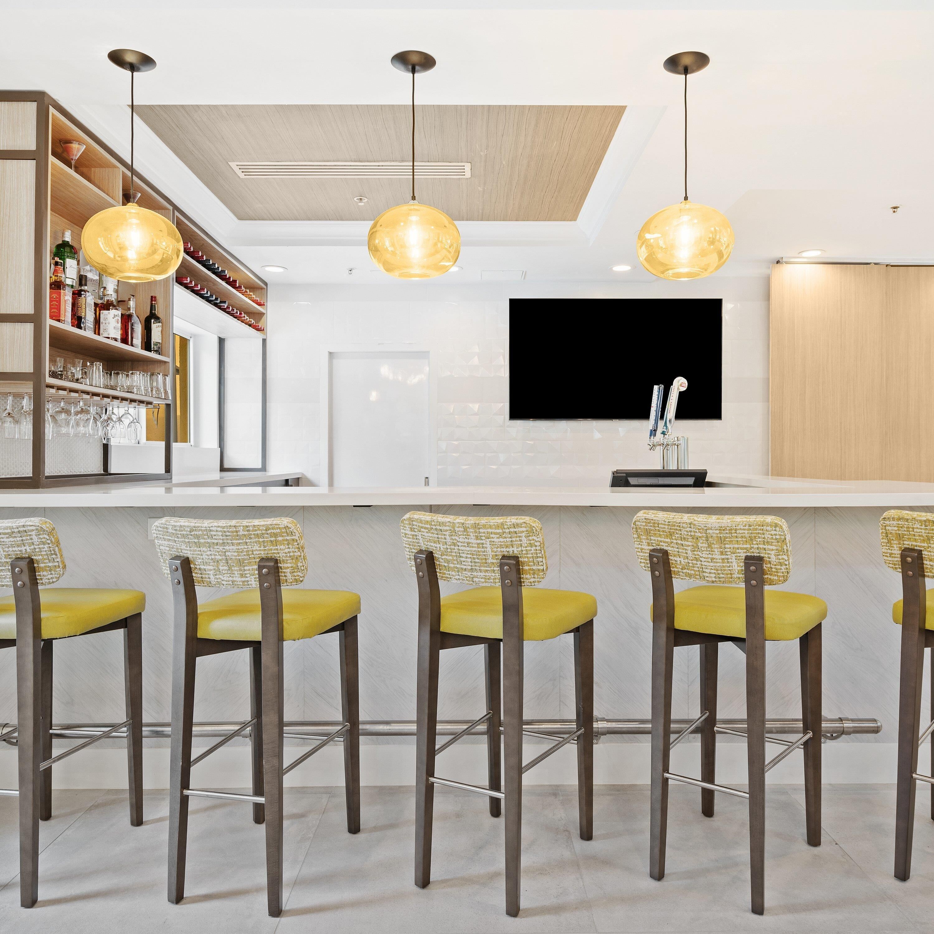 A modern bar area with a wooden ceiling, a mounted TV, and bar stools with yellow cushions.