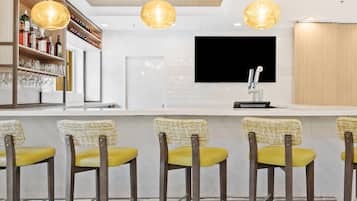 A modern bar area with a wooden ceiling, a mounted TV, and bar stools with yellow cushions.