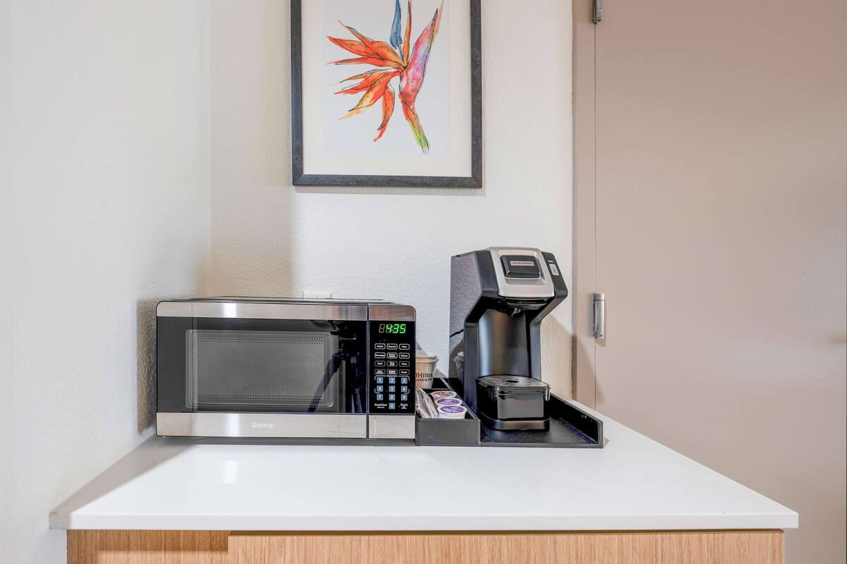 A kitchenette with a microwave, coffee maker, and a framed artwork on the wall.