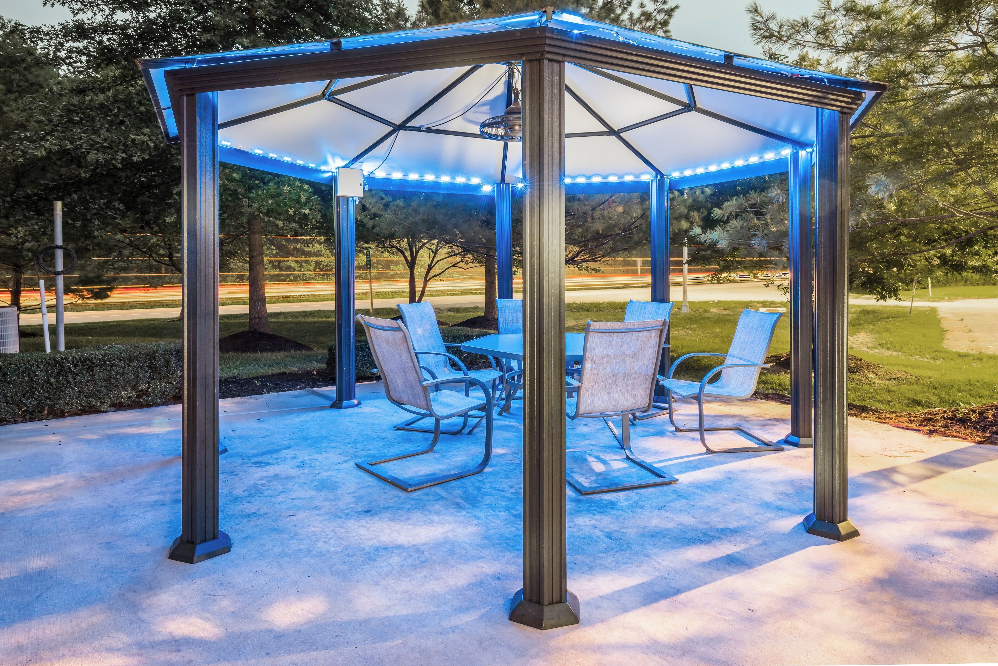 A gazebo with a transparent roof and blue LED lights, surrounded by outdoor furniture.