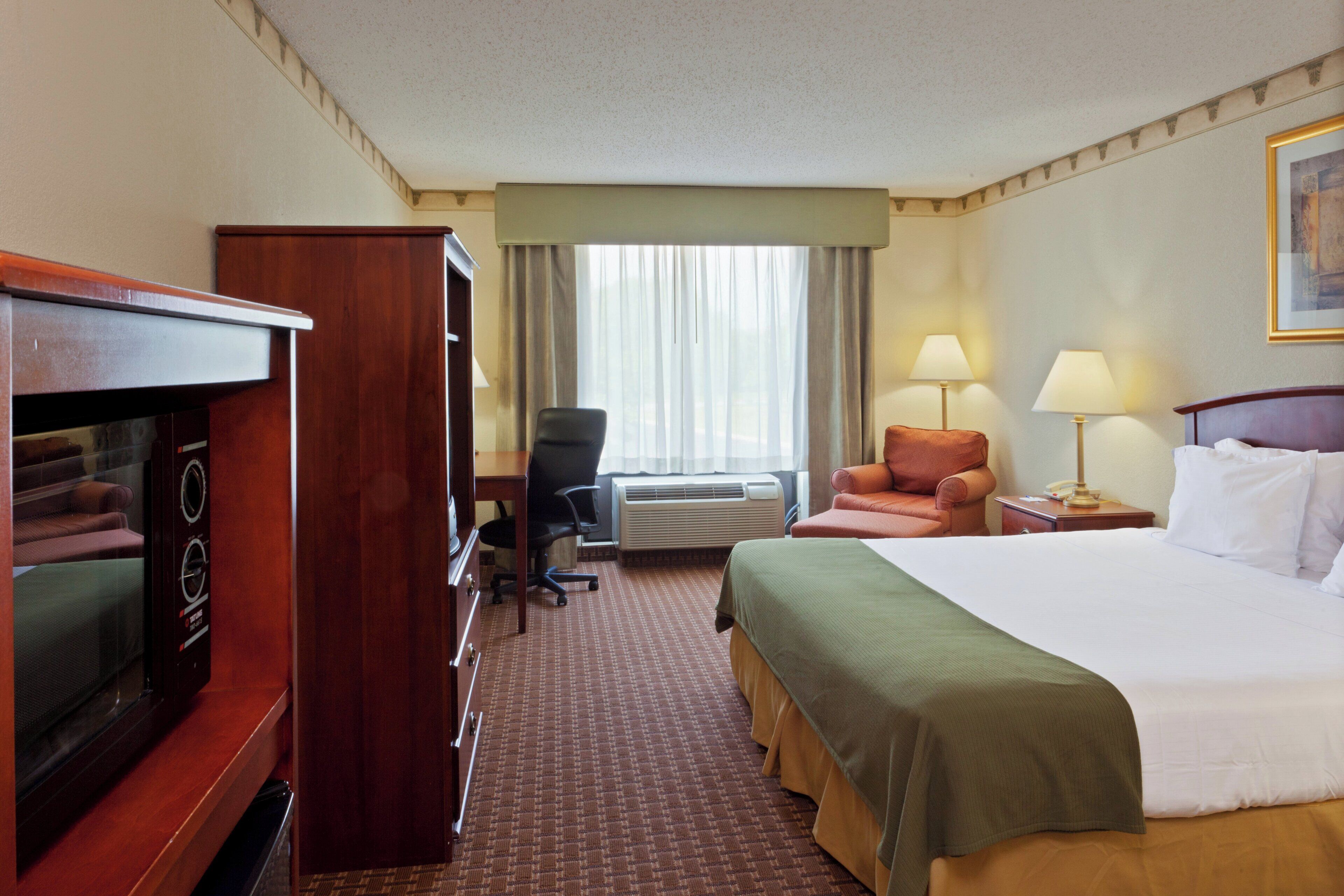 A hotel room with a bed, a desk, a chair, a television, and an air conditioning unit.