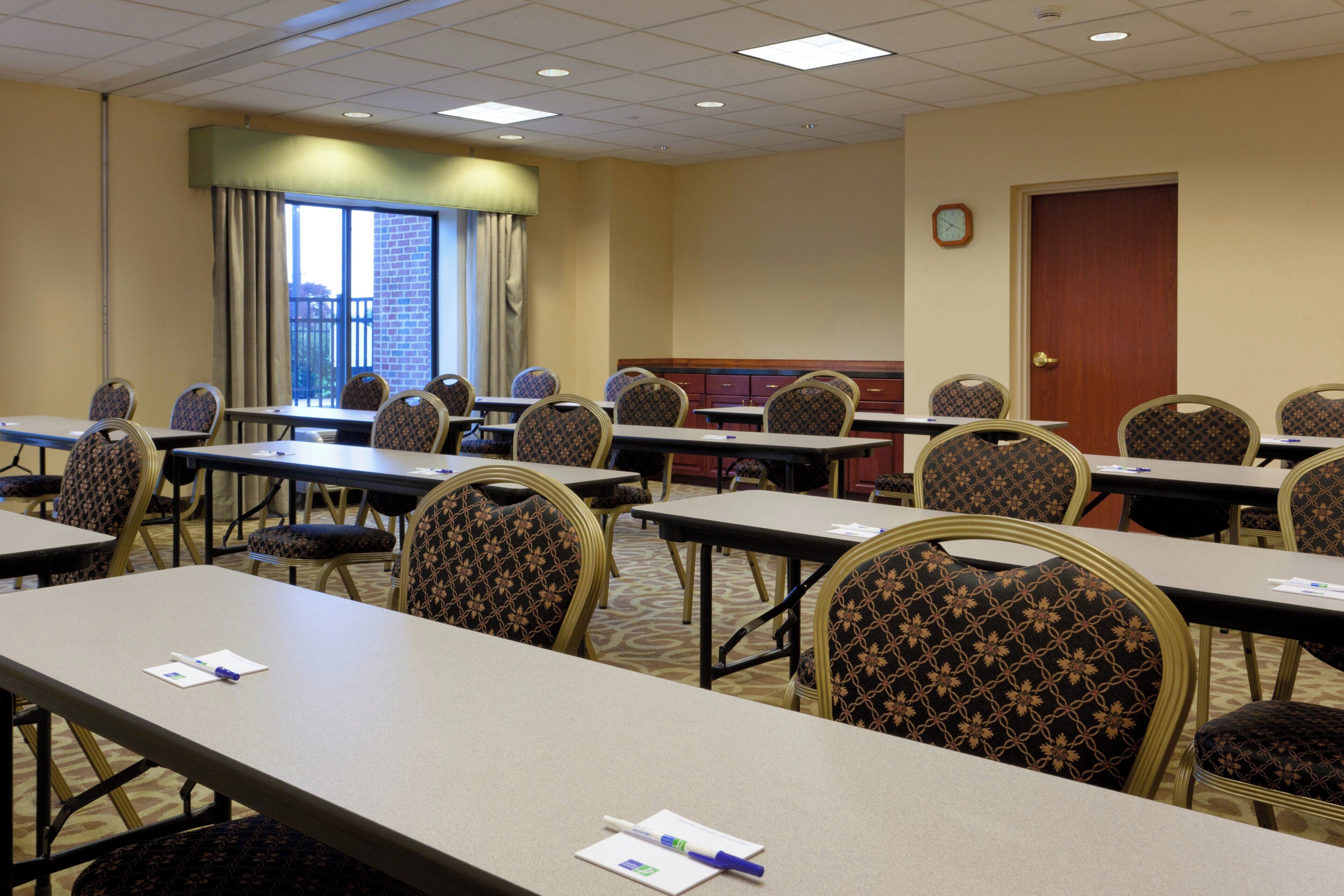 A conference room with multiple tables and chairs, a clock on the wall, and a window with curtains.