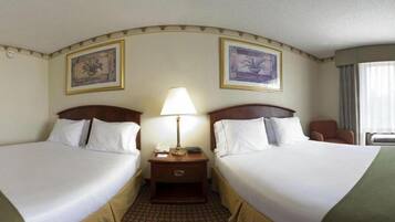 A hotel room with two beds, a nightstand with a lamp, and two framed pictures on the wall.