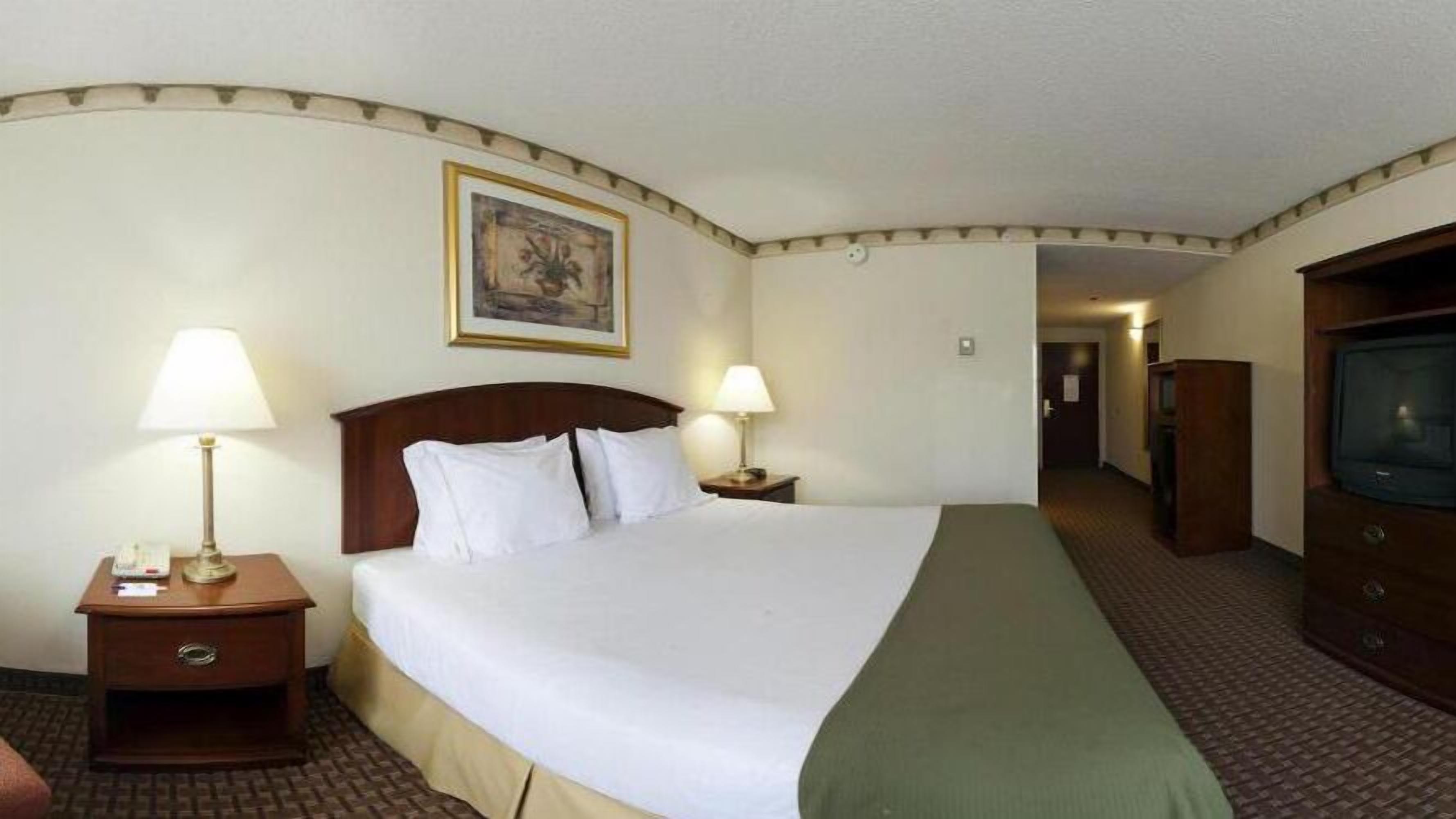 Une chambre d’hôtel avec un grand lit, deux tables de chevet avec des lampes, une télévision et un tableau encadré au mur.