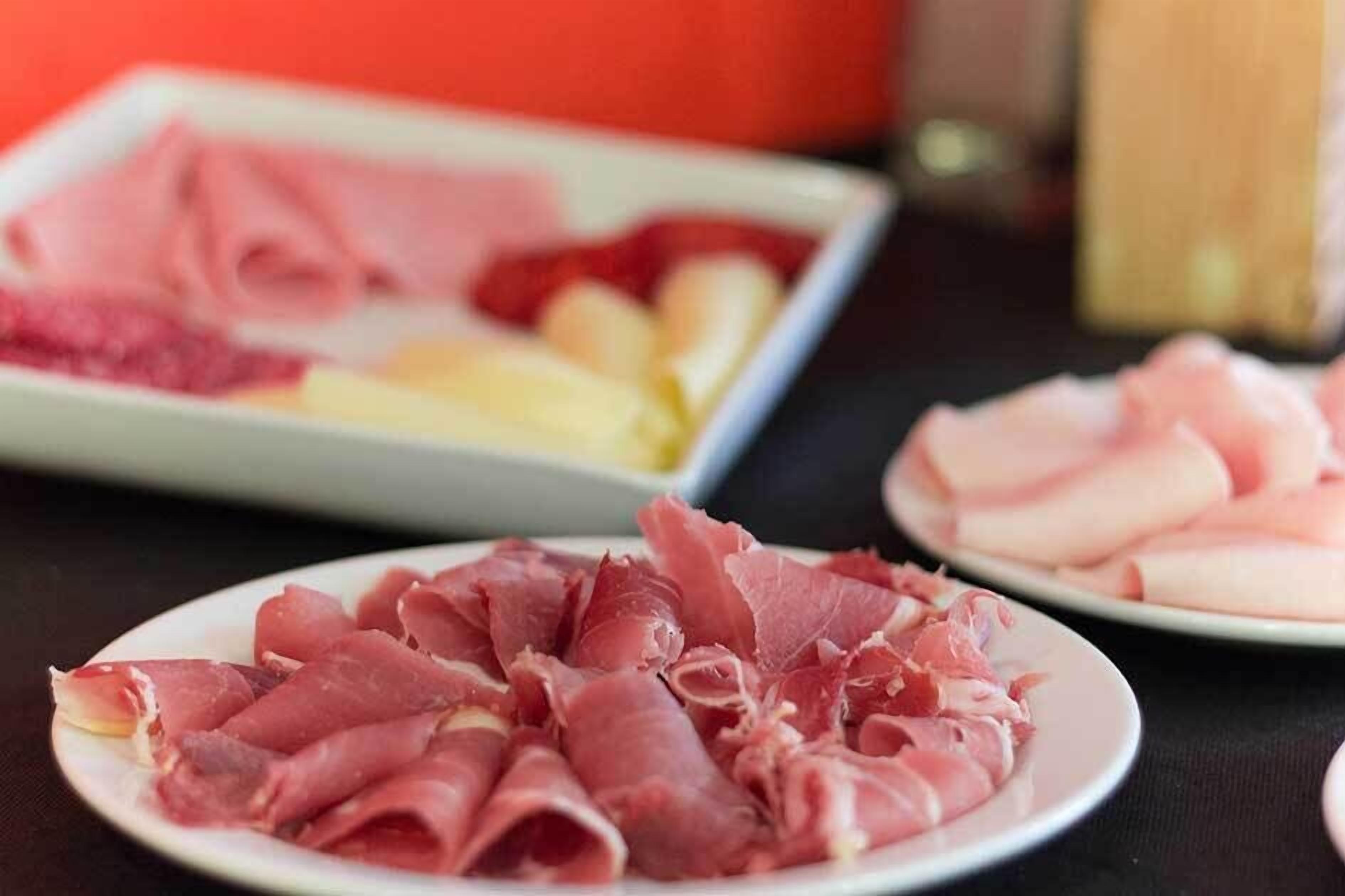 Una mesa con platos de embutidos en rodajas, incluyendo prosciutto y salami.