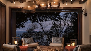 A cozy outdoor seating area with wooden furniture and a central table, overlooking a scenic view of trees and a body of water at dusk. - Four Seasons Resort Peninsula Papagayo, Costa Rica (Nacascolo)