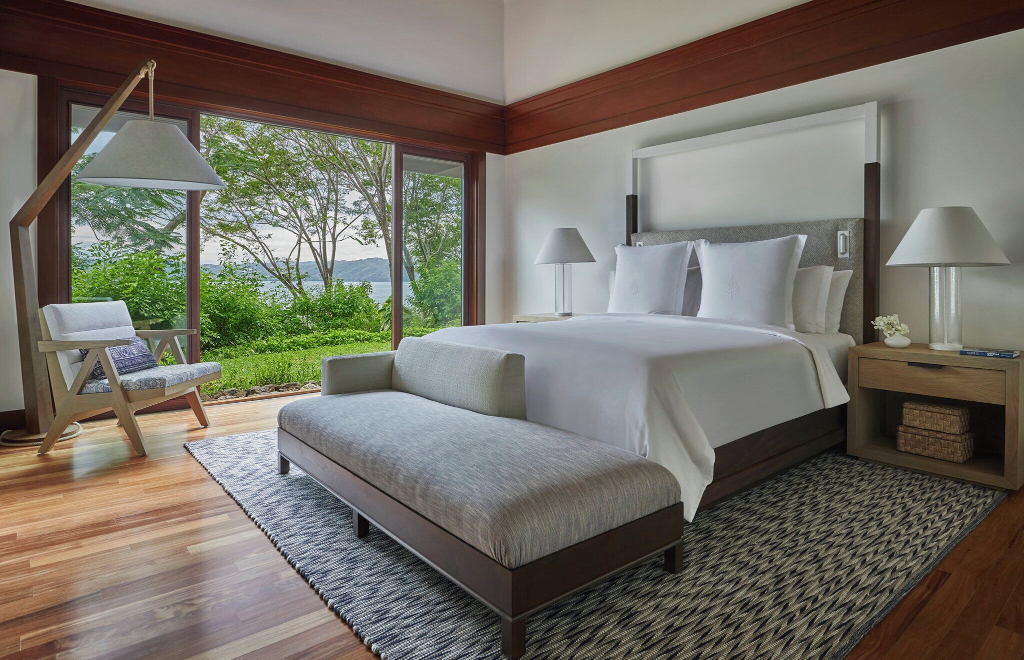 Un dormitorio moderno con una cama grande, un rincón de descanso y vistas a zonas verdes.