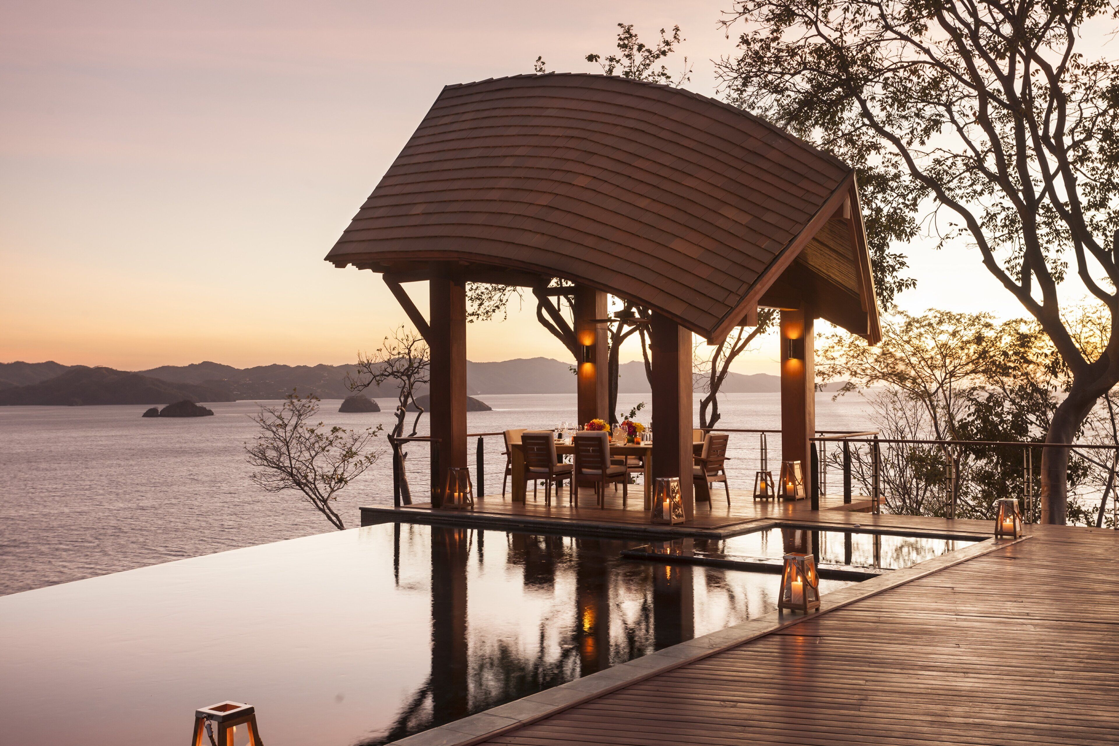 Une piscine à débordement avec une terrasse en bois et un belvédère offrant une vue sur une étendue d’eau.