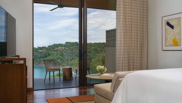 A bedroom with a large bed, a TV, and a view of a lush landscape through a sliding glass door.