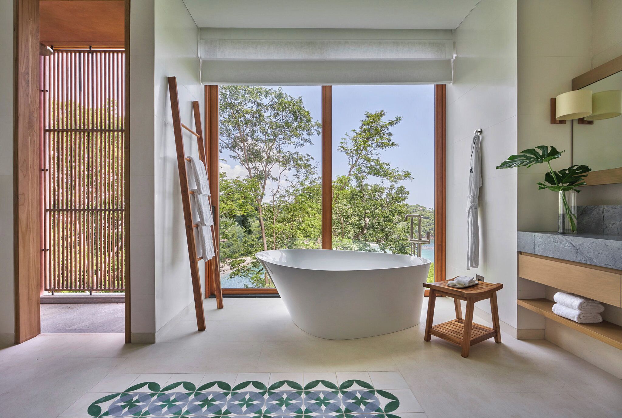 A modern bathroom with a freestanding bathtub, large windows, and a view of greenery.