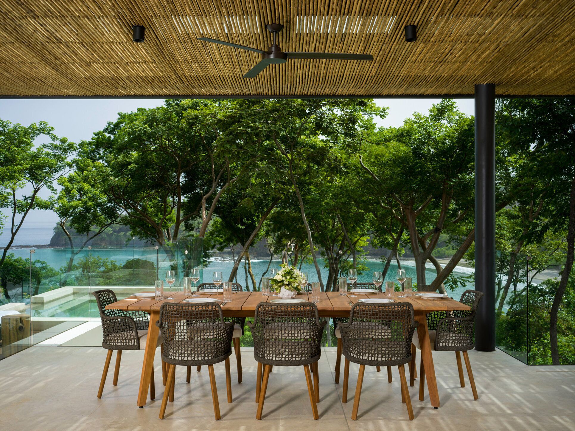 Un espace de restauration en plein air avec une table en bois et des chaises en osier, offrant une vue sur la côte.