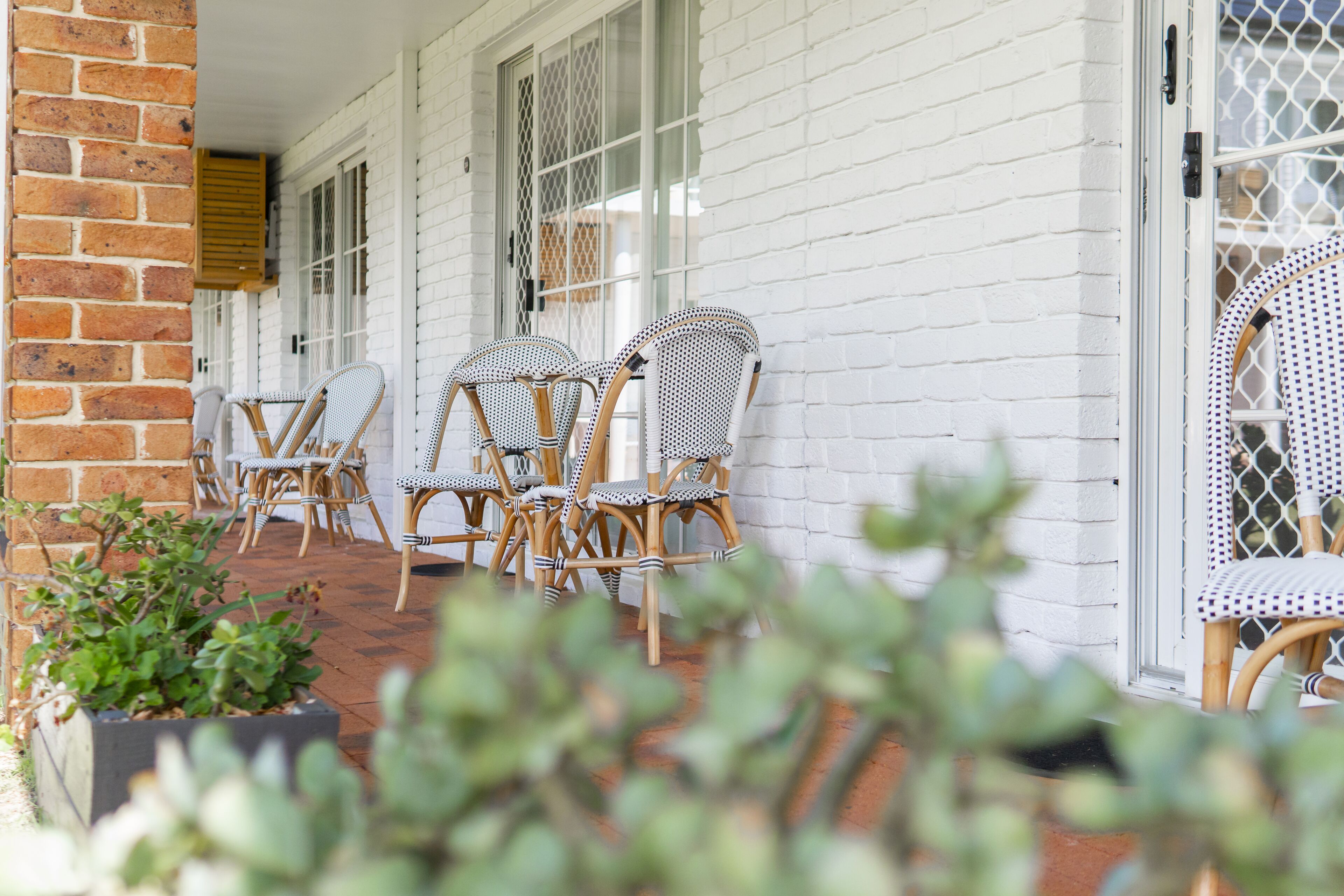A covered outdoor seating area with wicker chairs and a brick wall.