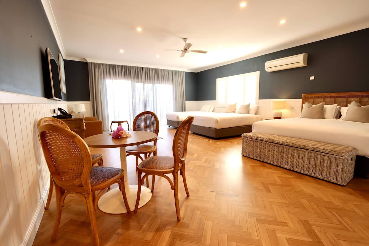 A hotel room with a dining area, a sofa set, a ceiling fan, and an air conditioning unit.