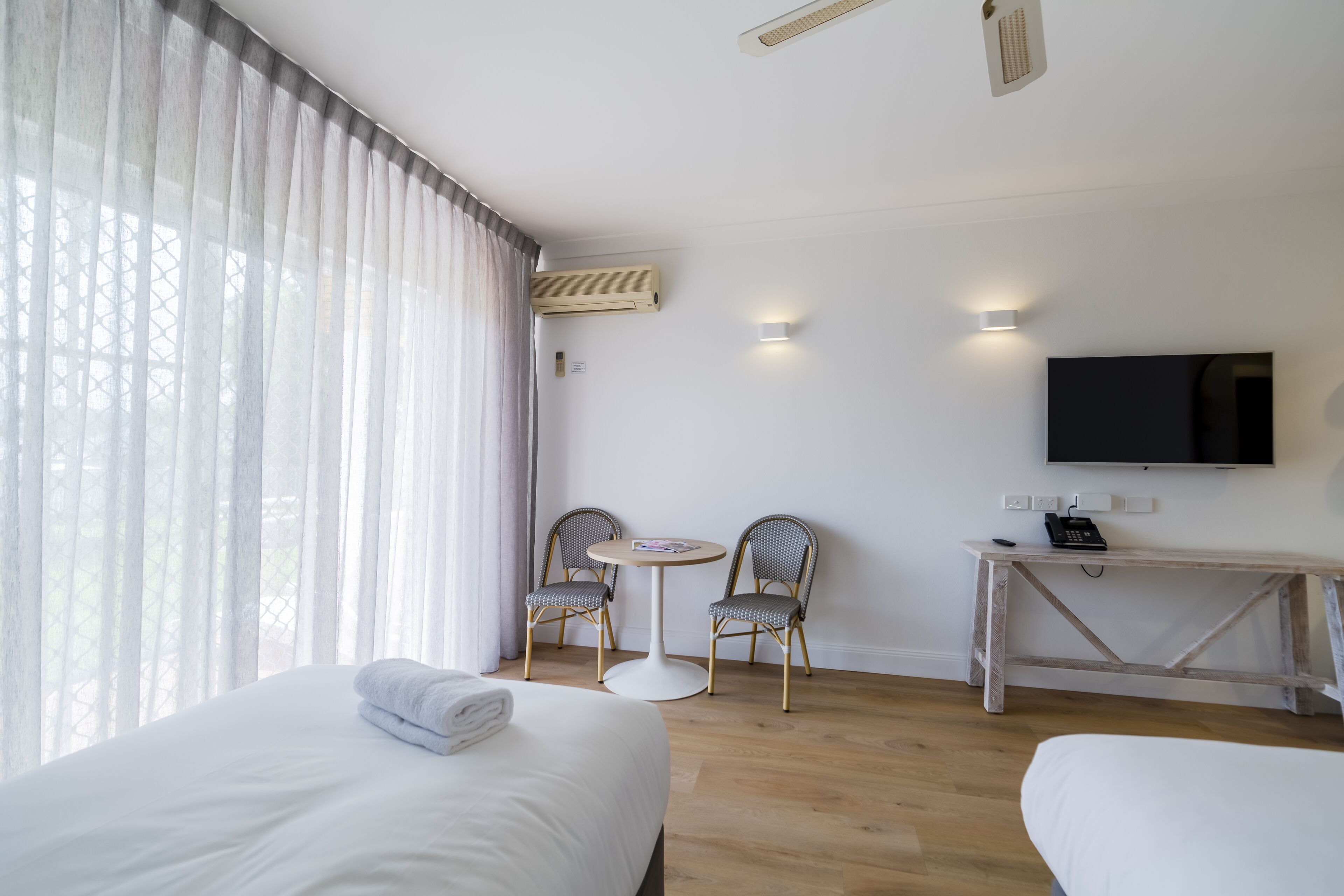 A hotel room with two beds, a desk with a TV, and a small table with chairs.
