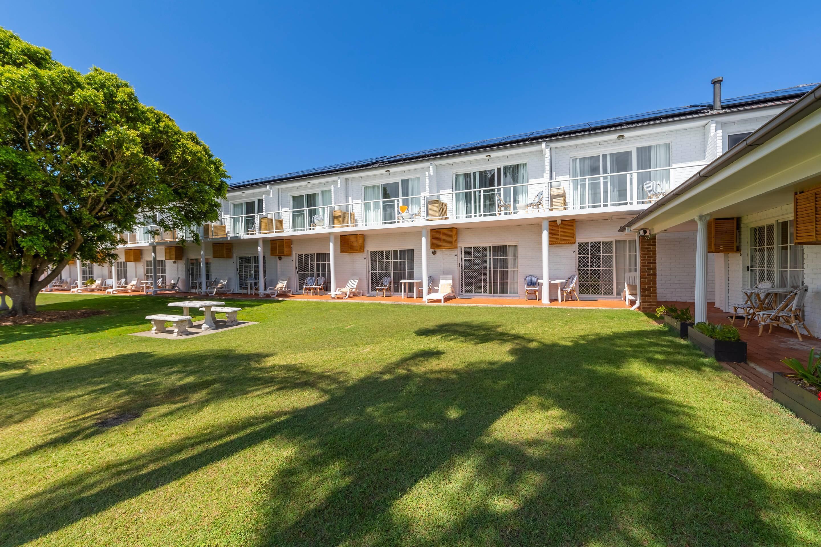 Un hotel con un patio amplio, asientos exteriores y un gran árbol que da sombra.