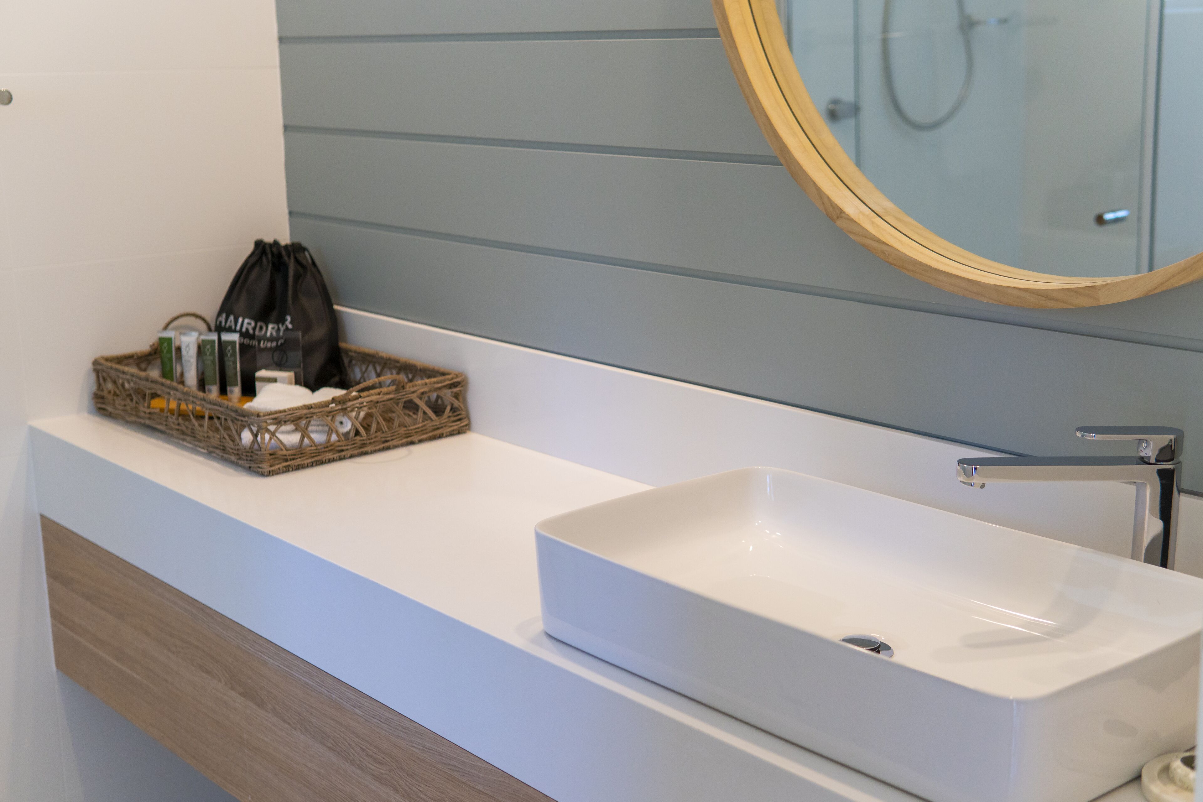 A bathroom with a white sink, a wooden vanity, a wicker basket with toiletries, and a mirror with a wooden frame.