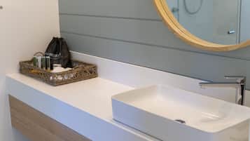 A bathroom with a white sink, a wooden vanity, a wicker basket with toiletries, and a mirror with a wooden frame.