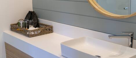 Une salle de bain avec un lavabo blanc, un meuble-lavabo en bois, un panier en osier contenant des articles de toilette et un miroir avec un cadre en bois.