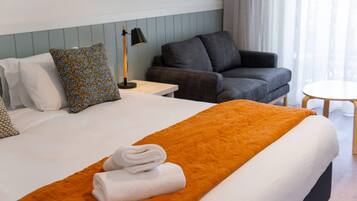 Une chambre d’hôtel avec un lit, un canapé gris, une petite table et une lampe.