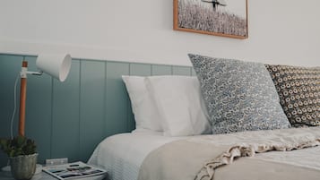 Une chambre à coucher bien rangée, avec un lit, des oreillers, une lampe de chevet, une petite table sur laquelle est posée une plante, et un tableau encadré accroché au mur.