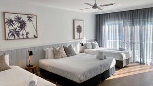 Habitación de hotel con dos camas, ventilador de techo y ventanas amplias con cortinas translúcidas.