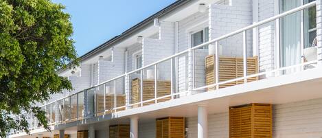 A hotel with a white exterior, multiple balconies, and outdoor seating areas with sun loungers.