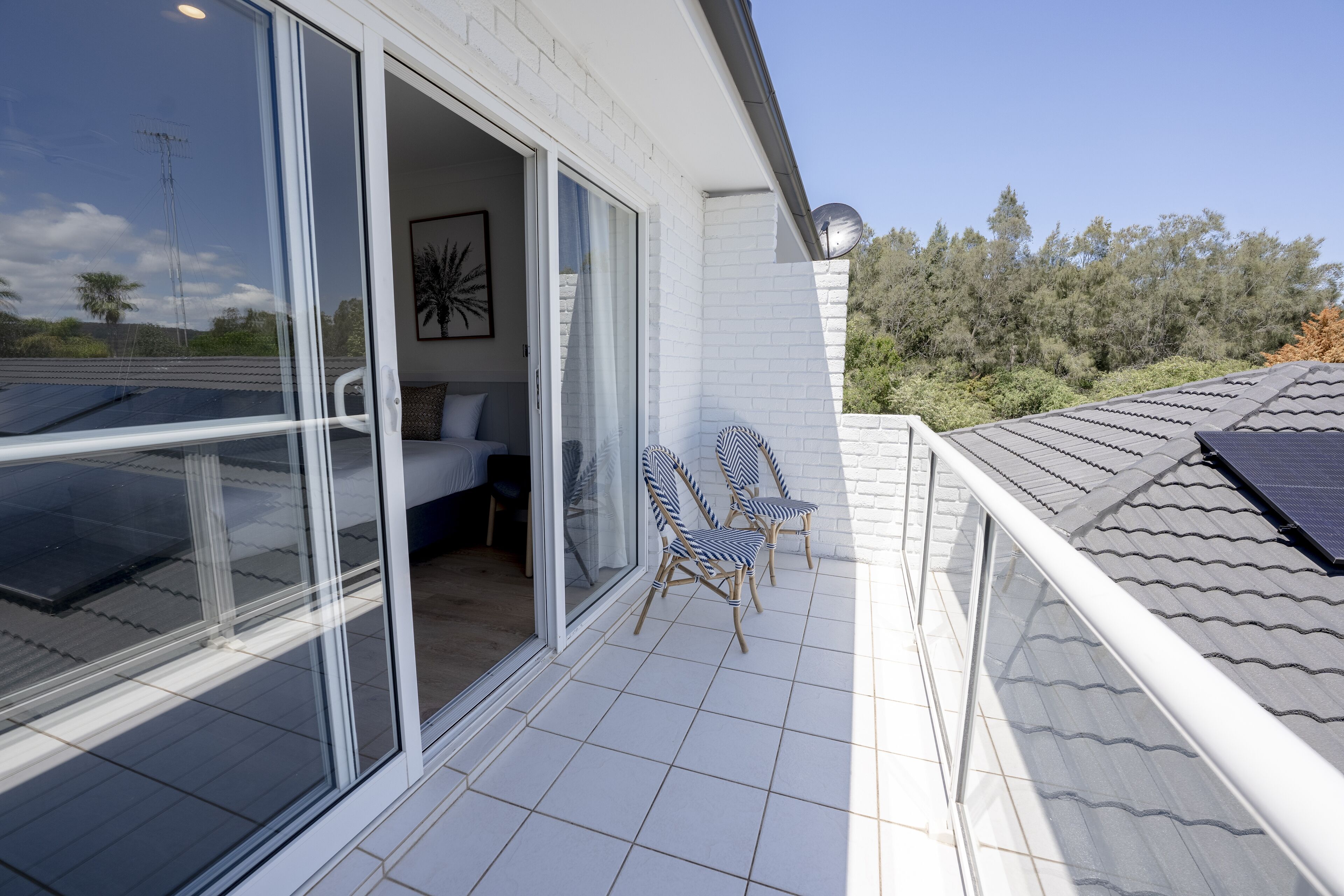 A modern house with a glass door leading to a patio area with two chairs and a sofa.