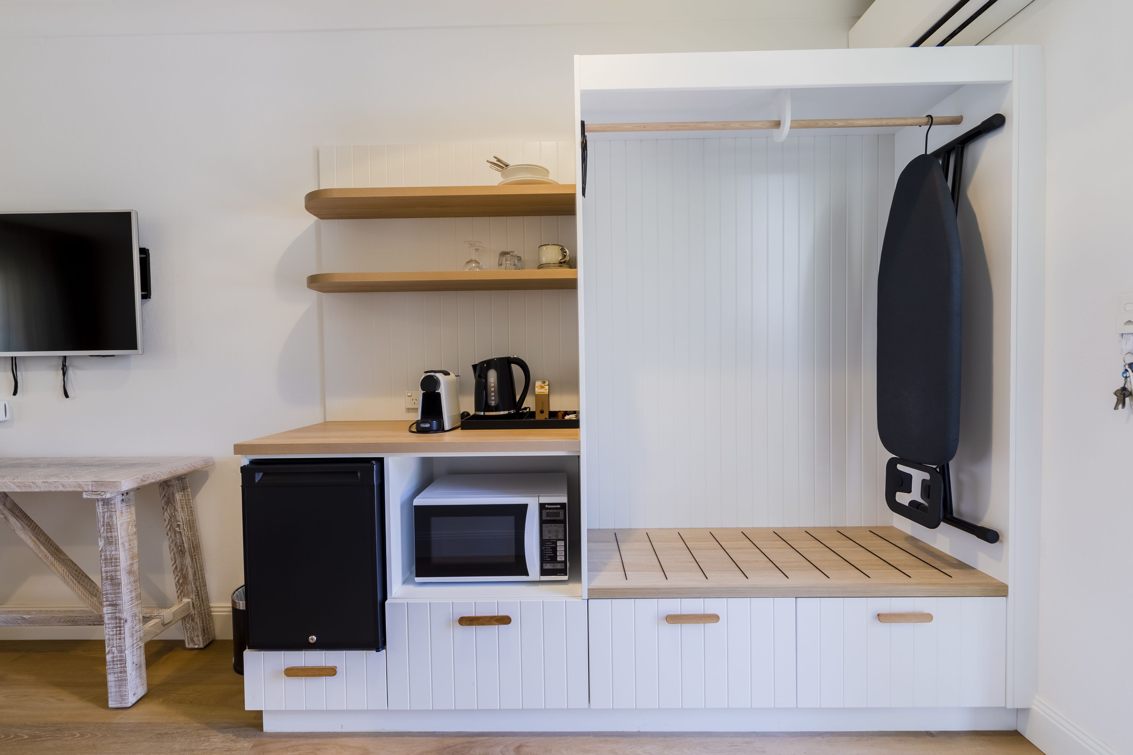 Una kitchenette compacta equipada con microondas, cafetera y tabla de planchar colgante.