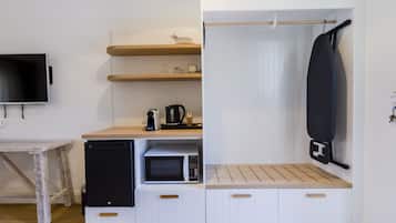 A compact kitchenette with a microwave, coffee maker, and a hanging ironing board.